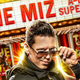 WWE superstar The Miz lowers his sunglasses and poses in front of a marquee and posters displaying his name.